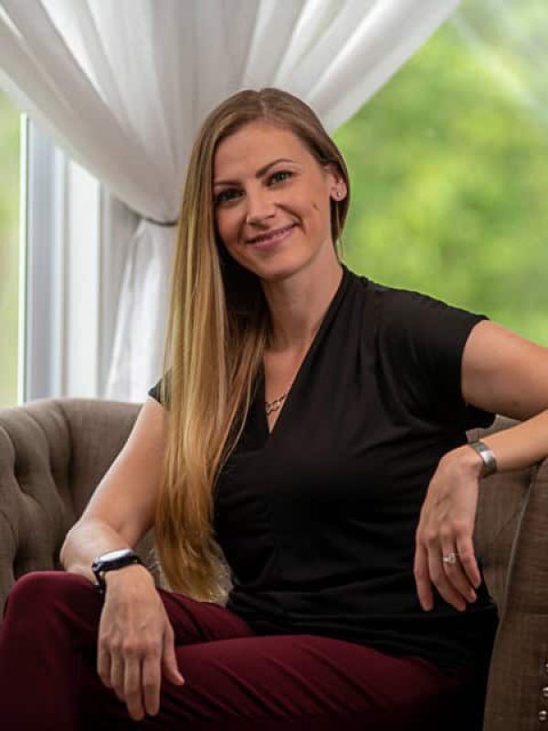 Dr. Aimee Vaughn, LPCC-S picture of woman in black shirt and red pants sitting in a chair in front of a window